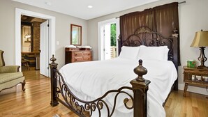 A bedroom with a large bed, wooden dresser, and a chair. - The Tailor House (Woodstock)