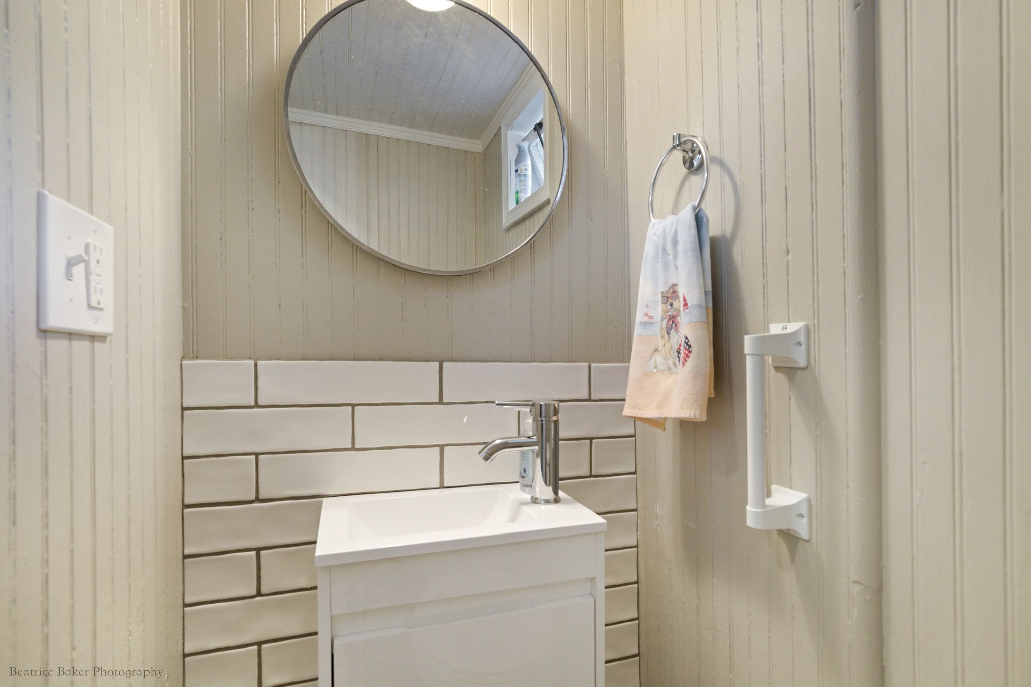A bathroom with a white sink, a round mirror, and a towel hanging on a metal ring.