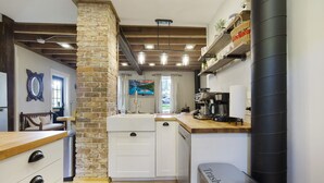 A compact kitchen with a stone column, wooden countertop, and a trash bin. - The Tailor House (Woodstock)