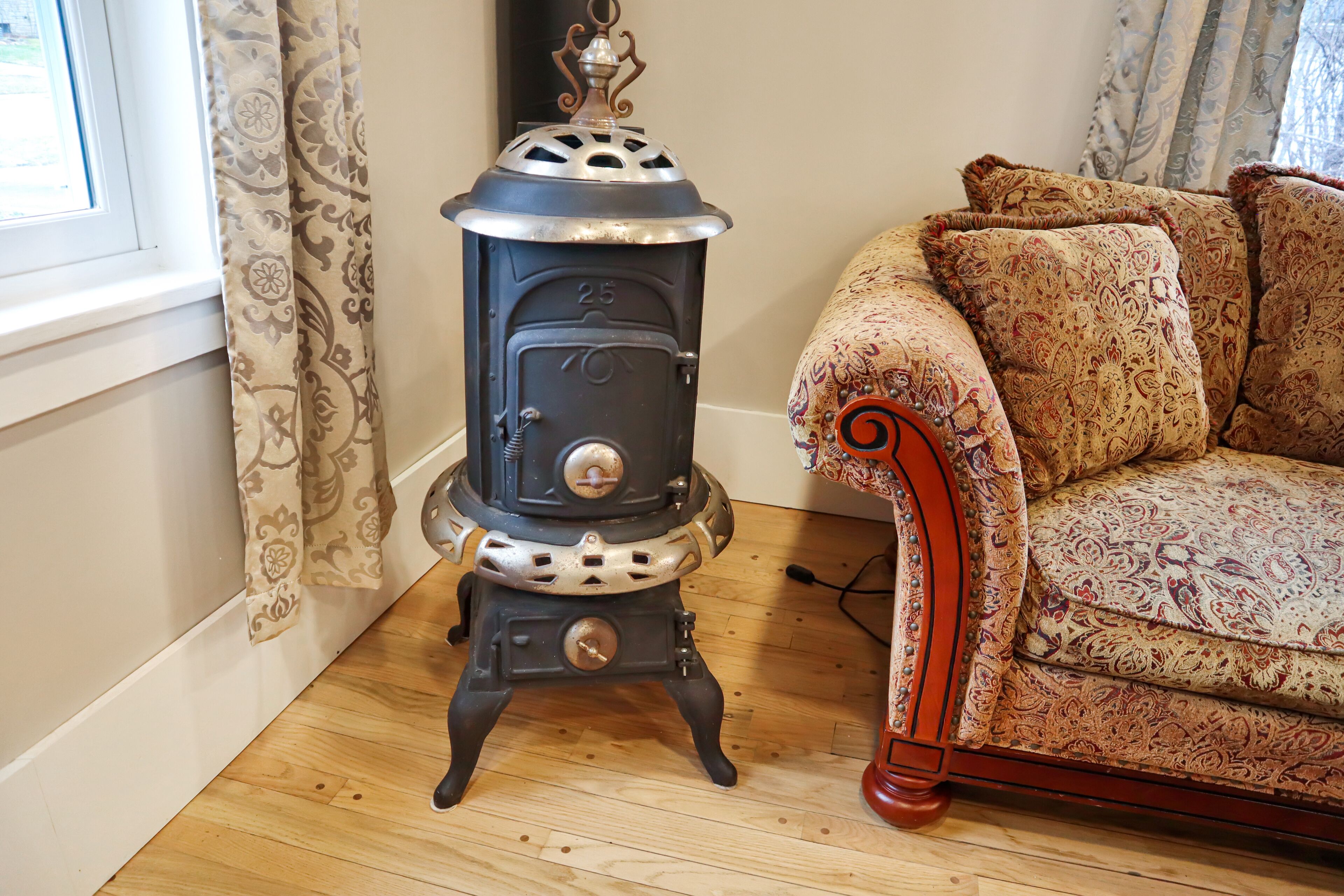 A vintage stove with a number "25" on it, placed next to a patterned sofa in a room with wooden flooring.