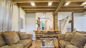 A cozy living room with a wooden ceiling, a dining area with a chandelier, and a staircase leading to another level. - The Tailor House (Woodstock)