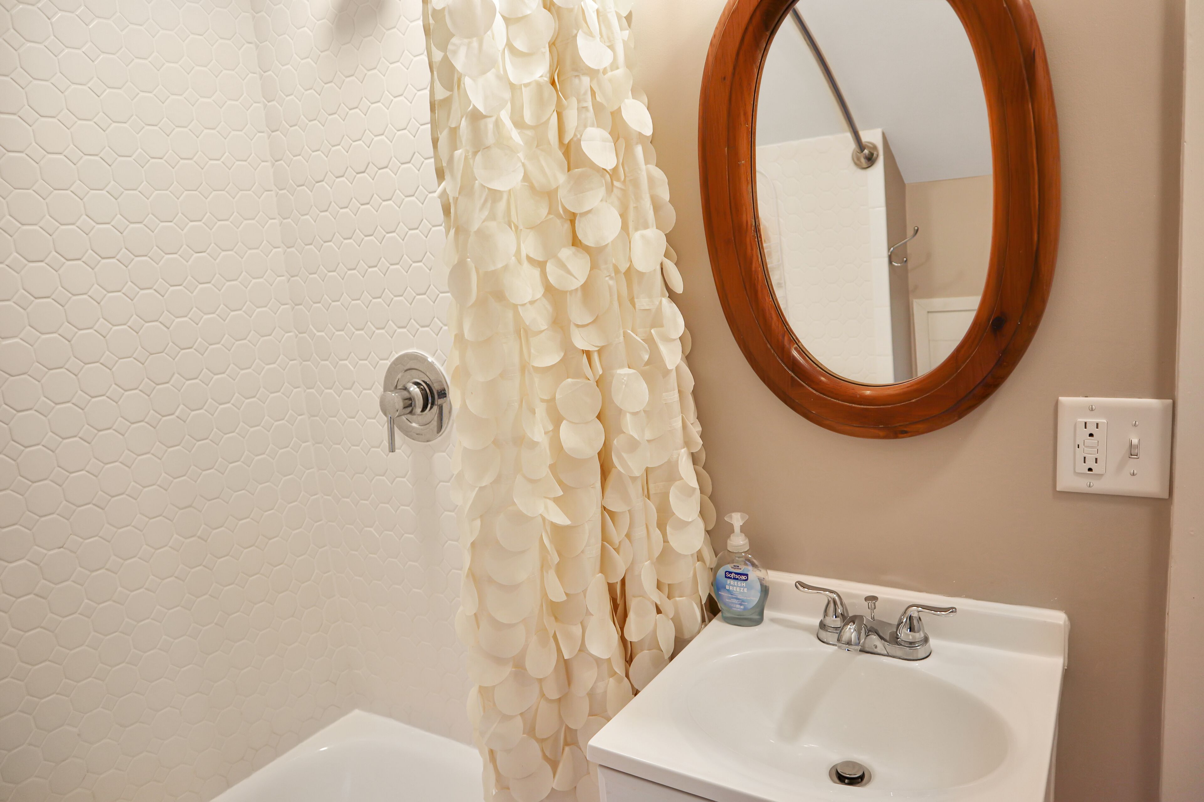 A bathroom with a white sink, a mirror with a wooden frame, and a shower curtain with a leaf pattern.