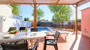 Un patio techado al aire libre con piscina, mesa de comedor y sillas.