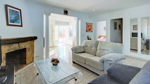 Una sala de estar con chimenea de piedra, un sofá color crema, un sillón gris y una mesa de centro de mármol.