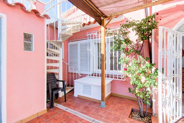 A pink building with a covered patio, a white gate, and a small tree.