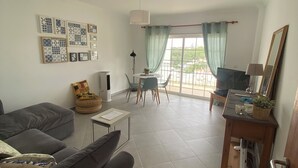 A living room with a sofa, a small table, a TV, and a balcony with a view.