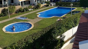 A residential area with two swimming pools, a well-maintained lawn, and houses with red-tiled roofs.