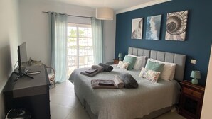 A bedroom with a bed, desk, chair, and a view of the outdoors.