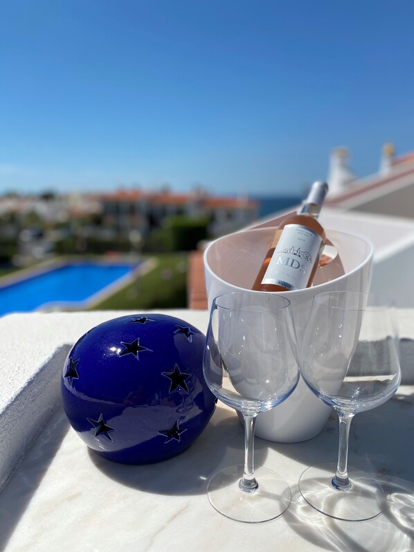 Une bouteille de vin dans un verre, posée sur un balcon avec vue sur la piscine.
