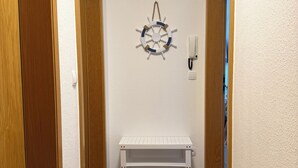 A hallway with wooden doors, a white bench, a wall-mounted light switch, and a wall decoration. - Luv & Lee Duhnen - Holiday apartment no. 5 near the beach (Cuxhaven)