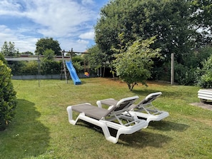 A grassy outdoor area with a blue slide, two lounge chairs, and a small tree. - Luv & Lee Duhnen - Vacation Apartment No. 5 Near the Beach (Cuxhaven)