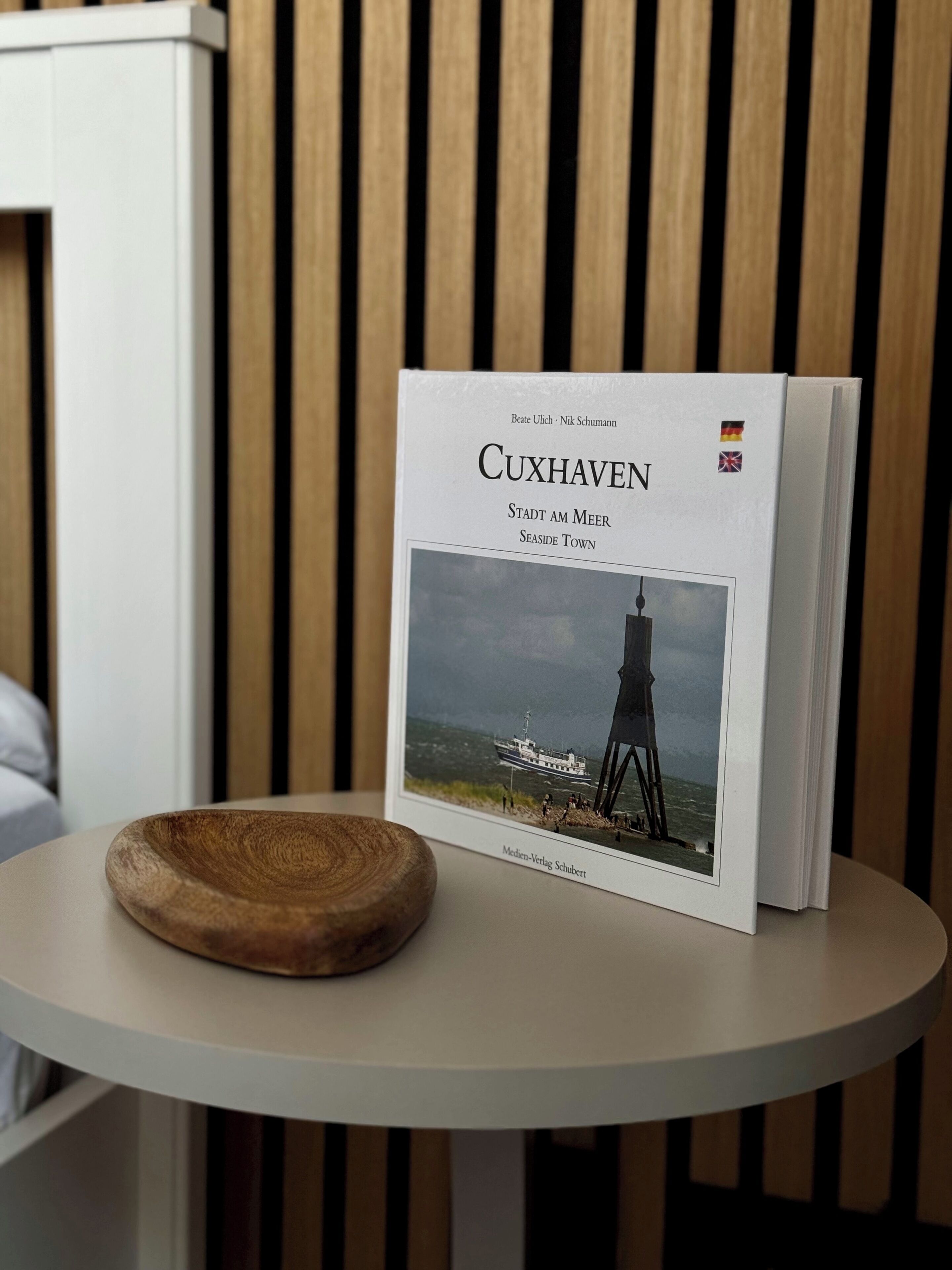A book titled 'Cuxhaven' on a white table against a wooden background.
