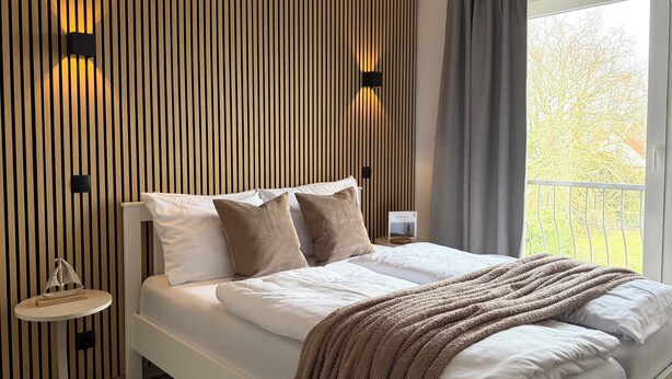 A modern bedroom with a bed, a bedside table, and a wall with vertical wooden slats. - Luv & Lee Duhnen - Holiday apartment no. 5 near the beach (Cuxhaven)