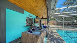 Ein überdachter Patio-Bereich mit Pool, Korbmöbeln und Blick auf den Garten.
