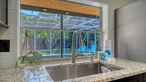 Eine Küche mit einer Spüle aus Edelstahl, einem Fenster mit Blick auf einen Garten und einem Fahrrad.
