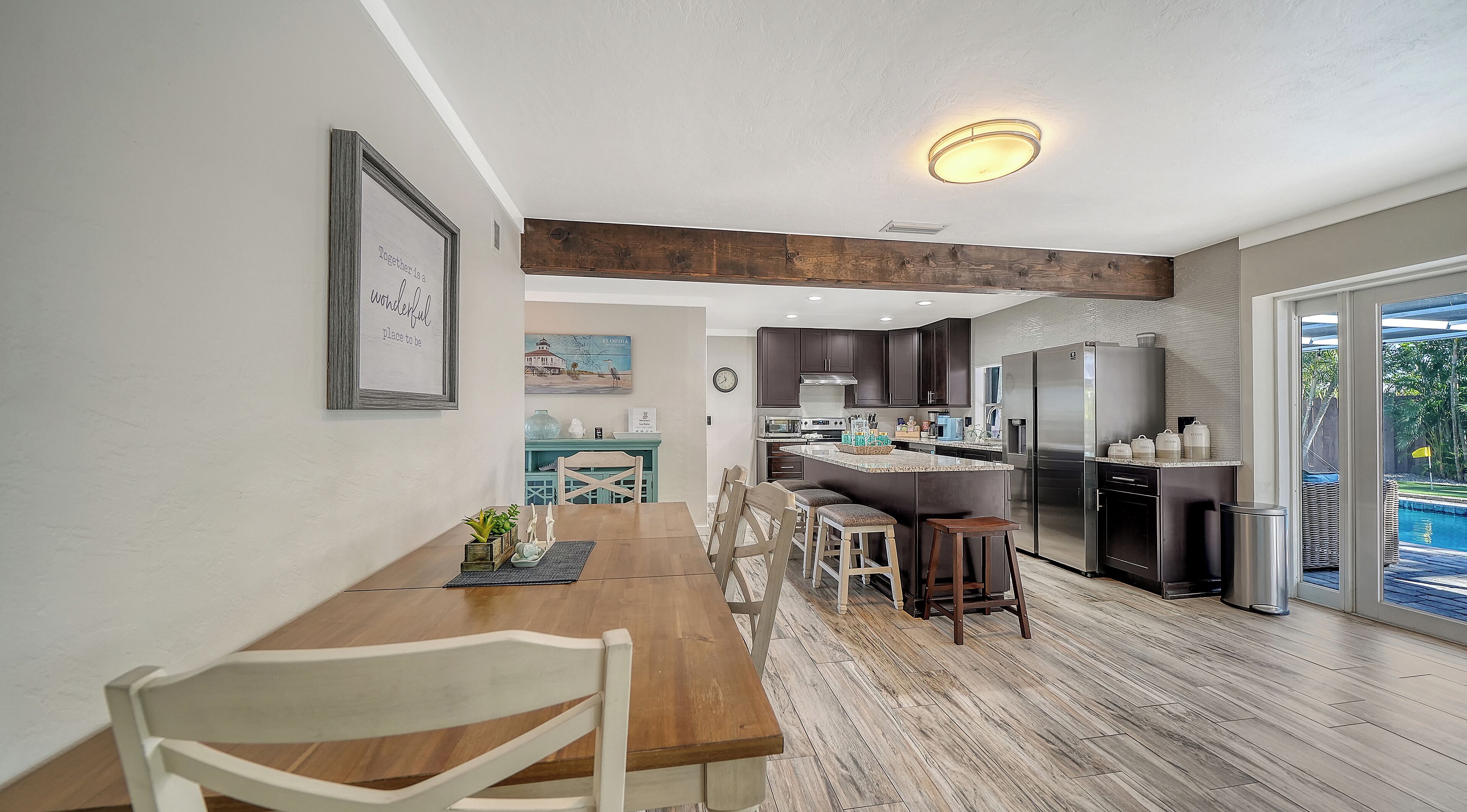 A modern kitchen with a central island, dark cabinets, stainless steel appliances, and a dining area with a wooden table and chairs.