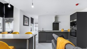 A modern kitchen with a central island, dark cabinetry, and a yellow throw on a grey sofa. - Winter Garden Apartments by Sasco (Blackpool)
