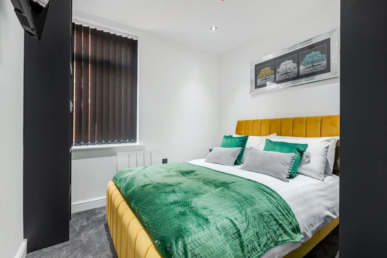 A bedroom with a bed, a window with blinds, a radiator, and a framed picture on the wall.