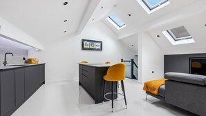 A modern kitchen with a central island, a dining area with a high ceiling and skylights, and a living area with a sofa and a TV. - Winter Garden Apartments by Sasco (Blackpool)