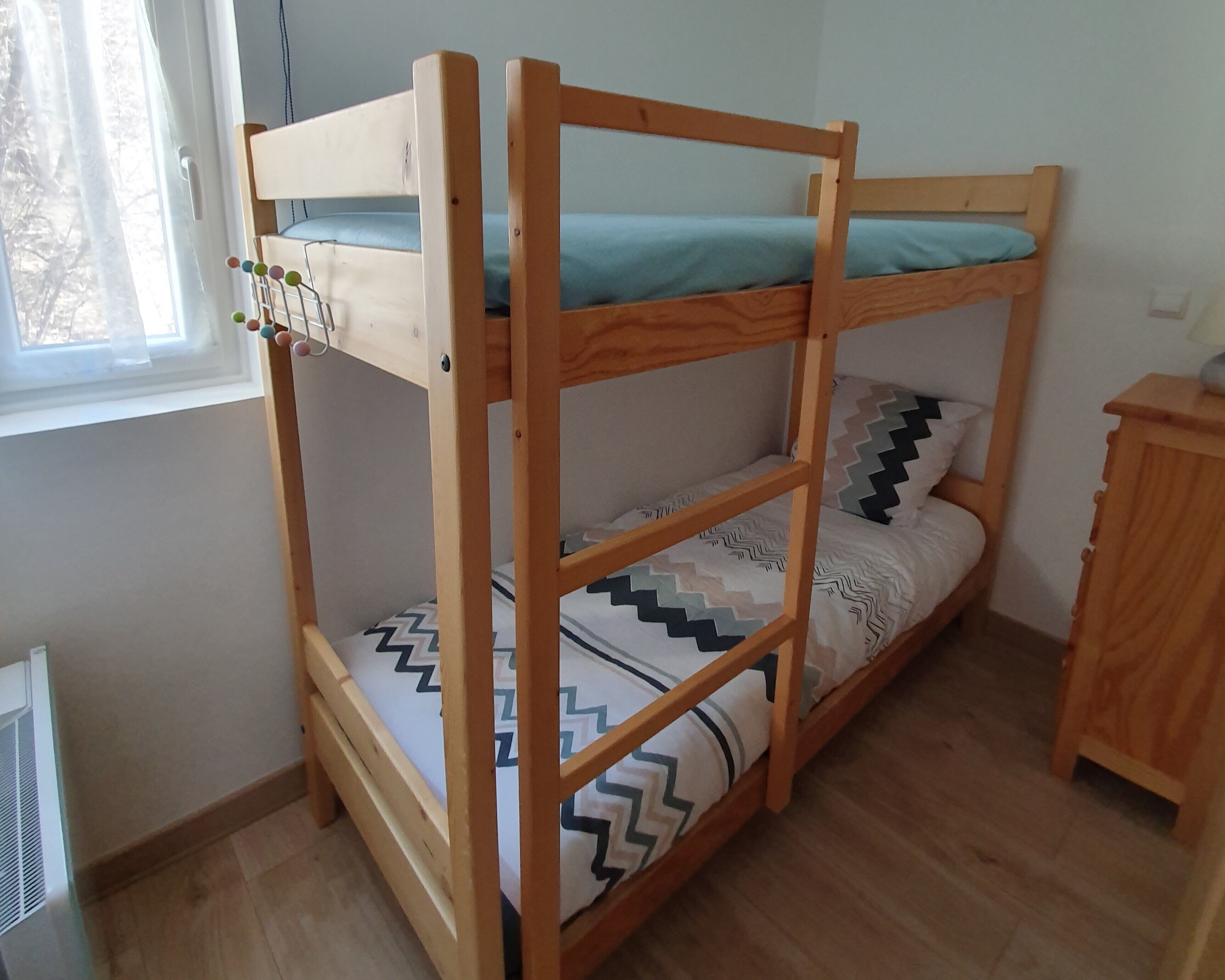 A bunk bed with a wooden frame, a window with curtains, and a radiator on the floor.