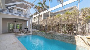 A swimming pool with a glass-enclosed deck, lounge chairs, and a view of palm trees. - Luxury Home in Naples with Private Pool & Walk to the Beach by Esthetic Stays (Naples)