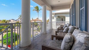 A covered outdoor seating area with white railings, a ceiling fan, and a view of palm trees and buildings in the background. - Luxury Home in Naples with Private Pool & Walk to the Beach by Esthetic Stays (Naples)