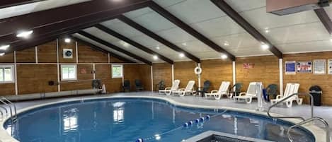 An indoor swimming pool with a diving area, lounge chairs, and a wooden wall.