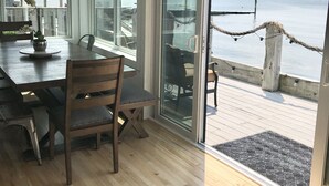A room with a wooden dining table, chairs, and a view of the sea through large windows. - Oceanfront Oasis Spacious 3-Bedroom, 2-Bath Retreat for 12  Linens Included (Old Saybrook)