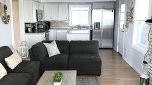 A modern living room with a sectional sofa, a coffee table, and a kitchen in the background. - Oceanfront Oasis Spacious 3-Bedroom, 2-Bath Retreat for 12  Linens Included (Old Saybrook)