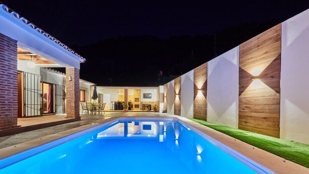 Ein Swimmingpool mit Terrassenbereich, ein Backsteinhaus und eine Holzwand mit integrierter Beleuchtung.