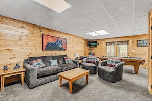 A cozy living room with a sofa, armchairs, a coffee table, a pool table, and a television.