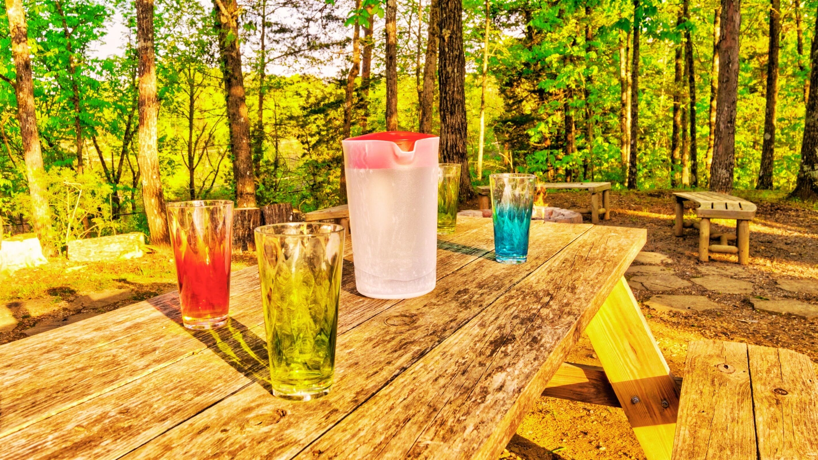 A picnic table with four glasses of different beverages.
