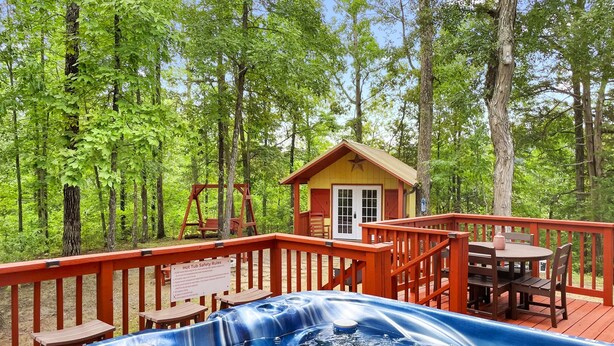 Ein Whirlpool, umgeben von einer Holzdielen-Terrasse, einer Holz-Schaukel und einer kleinen Holzhütte mit roter Tür und Fenstern.