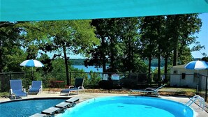 Una piscina con sillas de descanso y sombrillas, rodeada de árboles y vistas al agua.