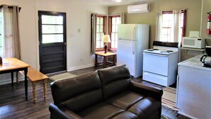 Un espacio habitable compacto con kitchenette, un sofá, una mesa de comedor y una puerta.