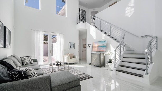 A spacious living room with a grey sofa, a coffee table, and a staircase leading to an upper level. - Beautiful Naples Home with Private Pool Near Beach & Dining by Esthetic Stays (Naples)