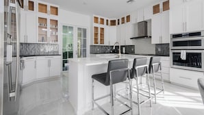 A modern kitchen with white cabinetry, a central island, and bar stools. - Beautiful Naples Home with Private Pool Near Beach & Dining by Esthetic Stays (Naples)