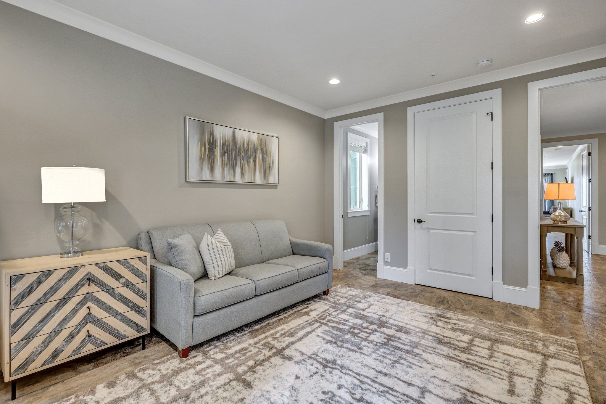 A living room with a gray sofa, a patterned sideboard, a large abstract painting, and a patterned rug.