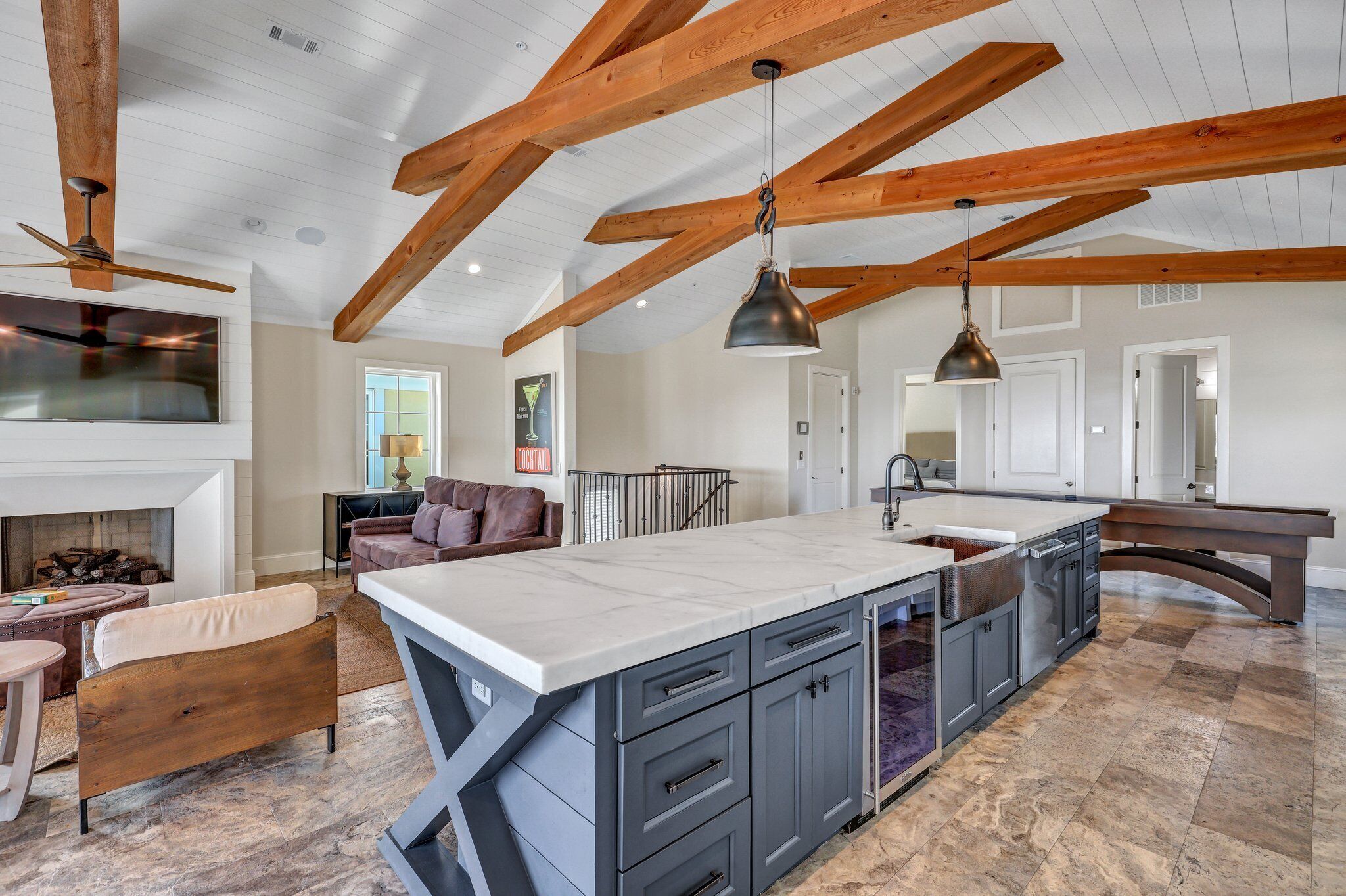 A spacious kitchen with a large island, wooden beams on the ceiling, and a fireplace.