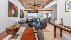 A spacious living area with a ceiling fan, a large window offering a city view, a dining table with chairs, and a sofa set. - Beautiful Sea of Cortes view Sandy Beach, Bella Vista (Puerto Peñasco)