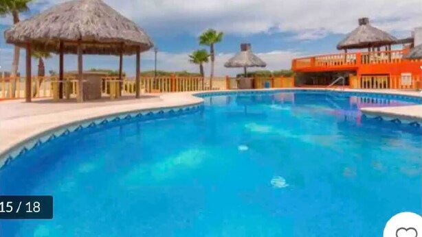 A swimming pool with a thatched-roof structure and a building in the background. - Beautiful Sea of Cortes view Sandy Beach, Bella Vista (Puerto Peñasco)