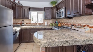 A kitchen with dark wooden cabinets, a granite countertop, a stainless steel refrigerator, a microwave, and a stove. - Beautiful Sea of Cortes view Sandy Beach, Bella Vista (Puerto Peñasco)