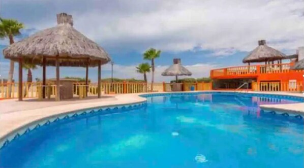 A swimming pool with a thatched-roof structure and a building in the background.