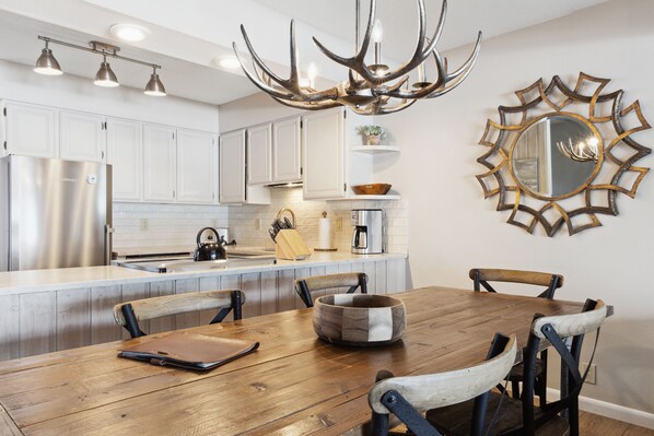 A modern kitchen with white cabinets, a wooden dining table, and a unique antler chandelier. - Outpost: Teton Shadows Granite E - Private Sauna! (Jackson)