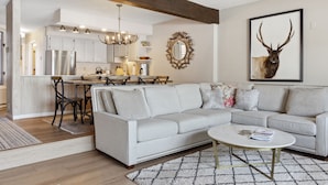A modern living room with a grey sofa, a coffee table, and a dining area with a chandelier. - Outpost: Teton Shadows Granite E - Private Sauna! (Jackson)