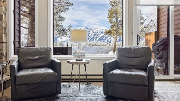 A room with two leather armchairs, a small table with a lamp, and a view of snow-capped mountains through large windows. - Outpost: Teton Shadows Granite E - Private Sauna! (Jackson)