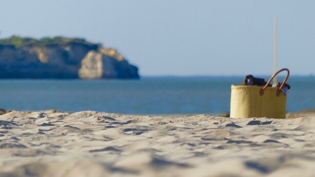 Una playa con un cubo amarillo que contiene una pajita y una bolsa.