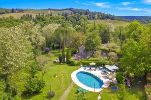A large, oval-shaped swimming pool surrounded by a well-maintained lawn and a variety of trees. - Molino del Ponte (Radda in Chianti)