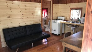 A compact cabin-style room with a sofa, a small kitchenette, and a wooden floor.