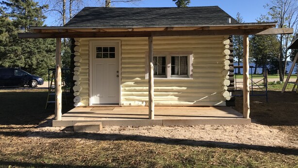 A log cabin with a front door, a small window, and a porch.